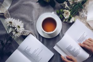 photo of open books with a cup of coffee on a table and flowers surrounding the books and coffee